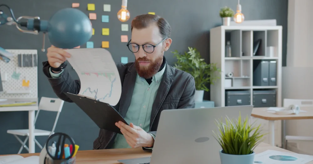 En person går igenom grafiskt underlag vid ett skrivbord